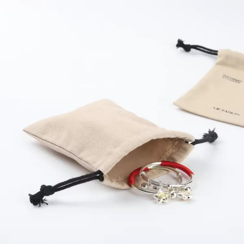 Natural cotton canvas drawstring pouches with black cords and jewelry at the open mouth