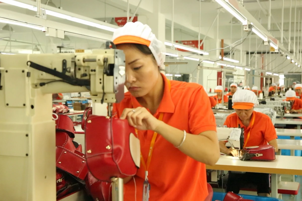 An operator sewing a red bag on an upright industrial sewing machine.