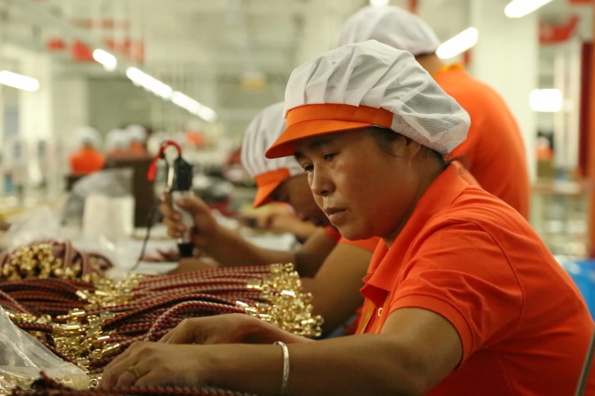 An operator working with bag handles and metal hardware at a worktable.