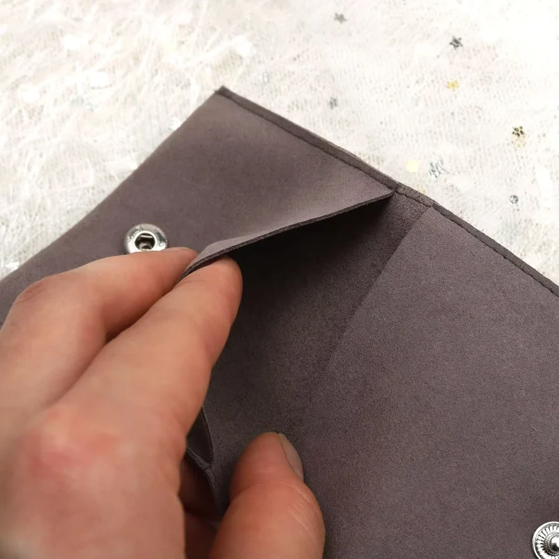 A hand opening the flap of a taupe jewelry pouch