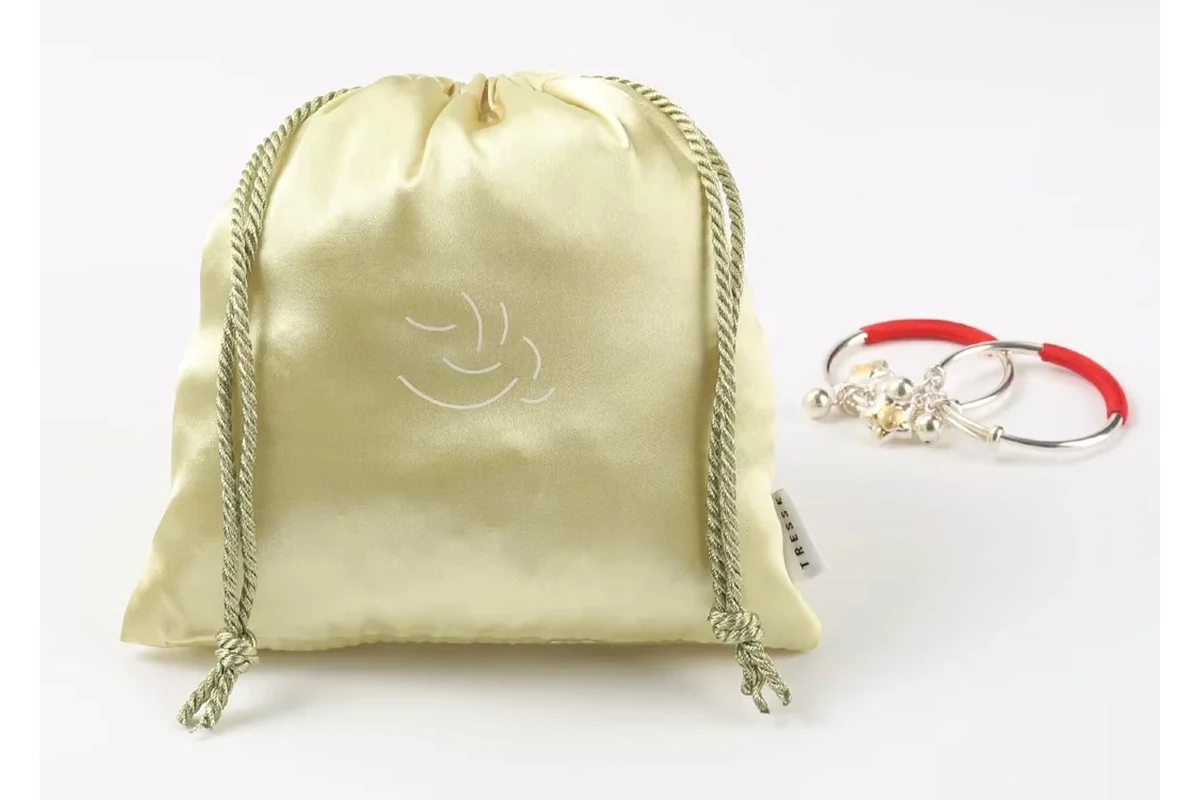 Pale yellow satin jewelry pouch with twisted drawstrings and a white curved motif