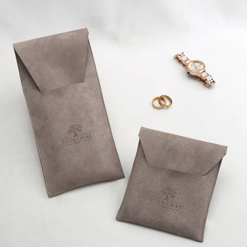 Taupe flap jewelry pouches in tall and square formats beside a watch and rings