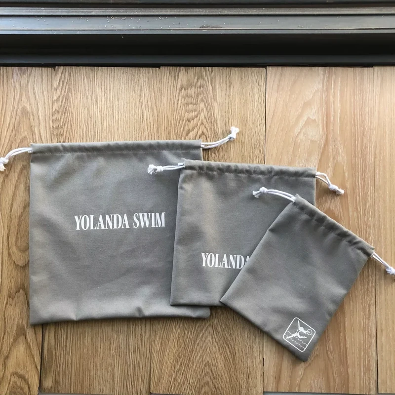 Gray cotton drawstring bags with white printed logos arranged flat