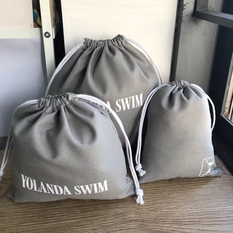 Three gray cotton drawstring bags with white cords and printed logos