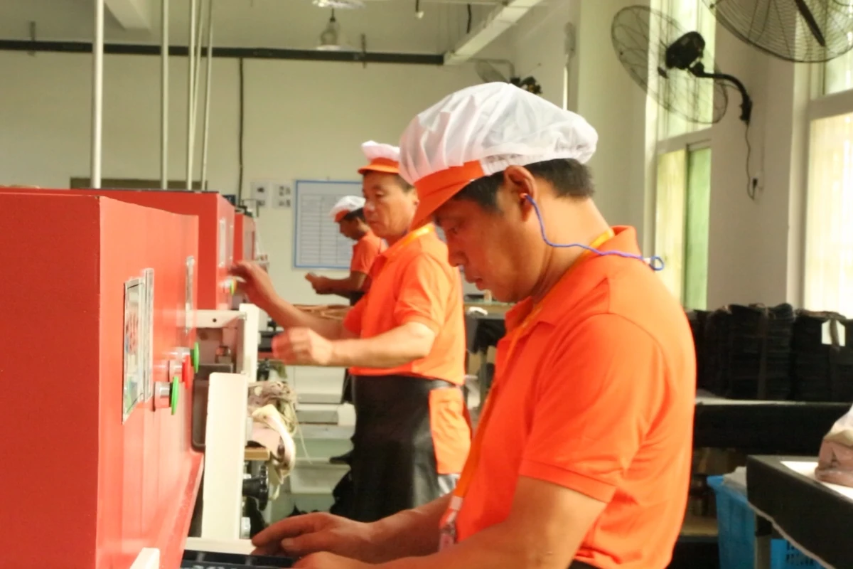 Operators handling bag components beside a row of red workshop machines.