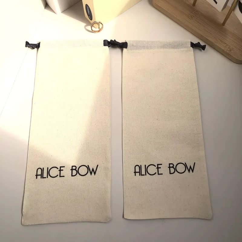 Two long natural cotton drawstring pouches laid flat with black ribbon ties and printed logos