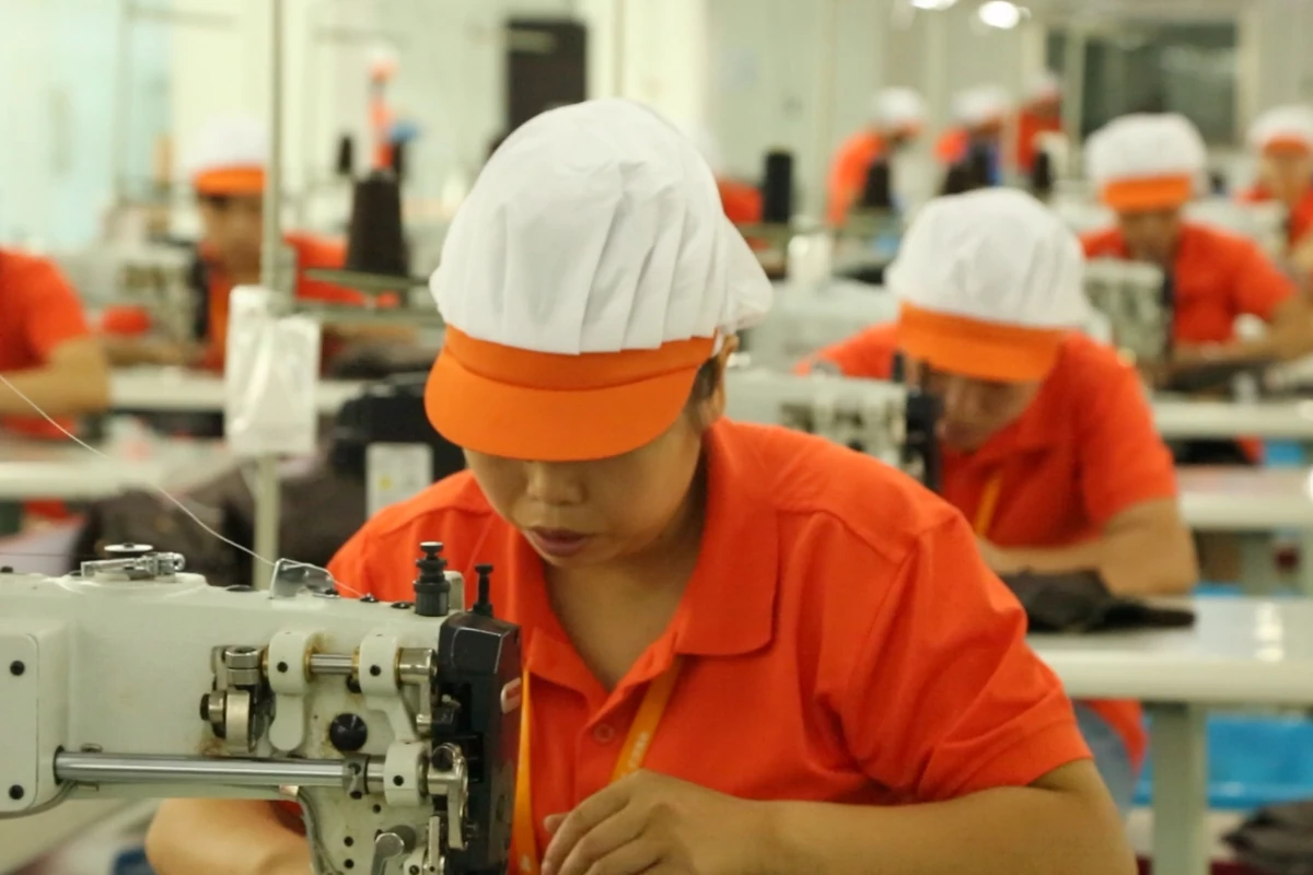 An operator guiding bag material through a sewing machine with more workstations behind.