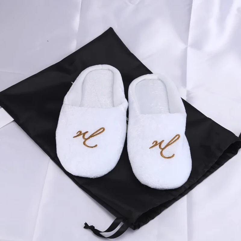 White embroidered slippers displayed on a black drawstring shoe bag.