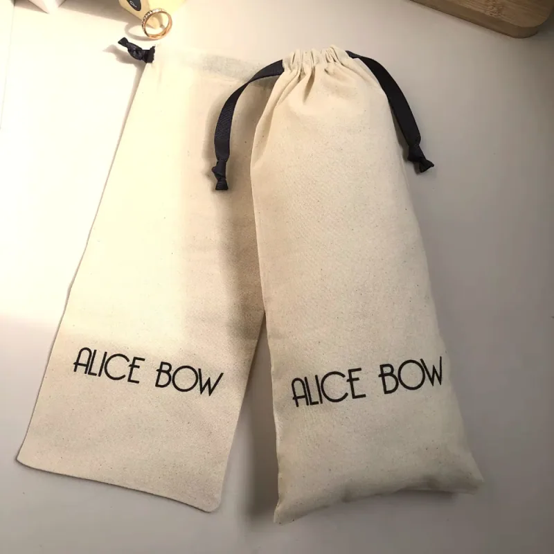 Two long natural cotton drawstring pouches with black ribbon ties and printed logos