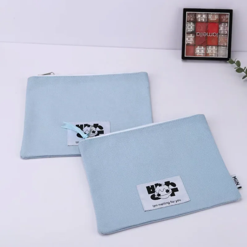 Two light blue flat accessory pouches with top zippers and fabric labels