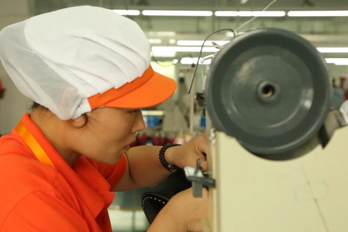 An operator working beside the handwheel of an industrial sewing machine.