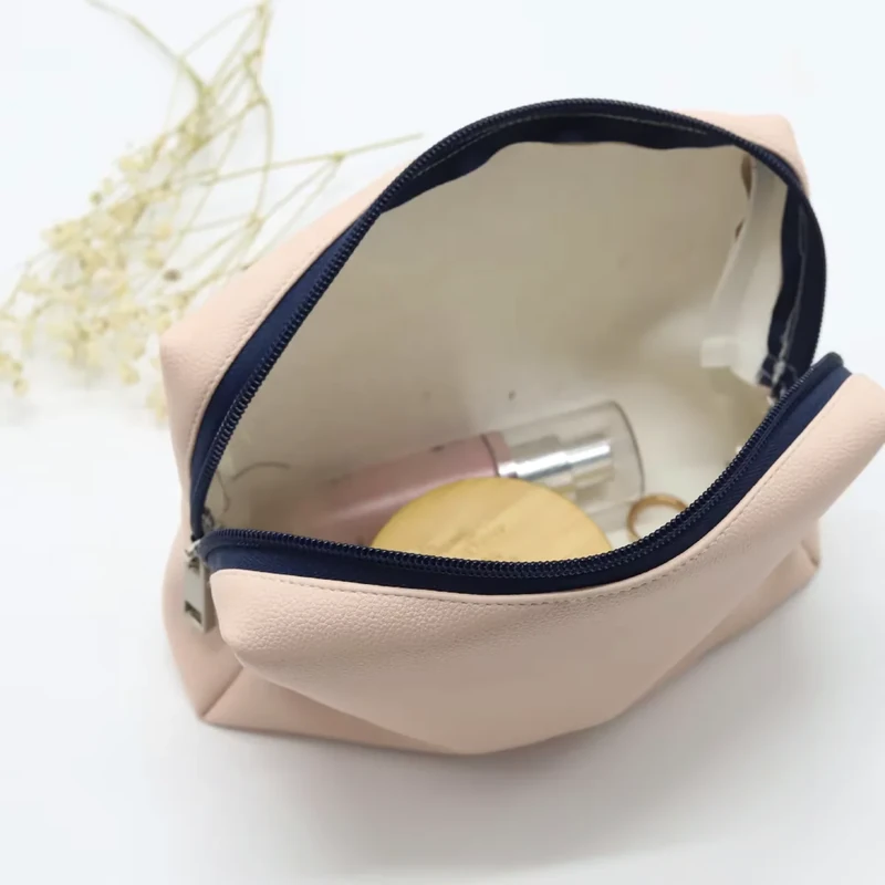 Open blush travel pouch with a navy zipper and cream lining holding cosmetics