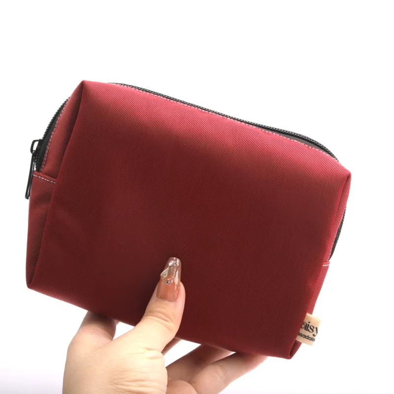 A red travel zipper pouch held to show its side and depth.