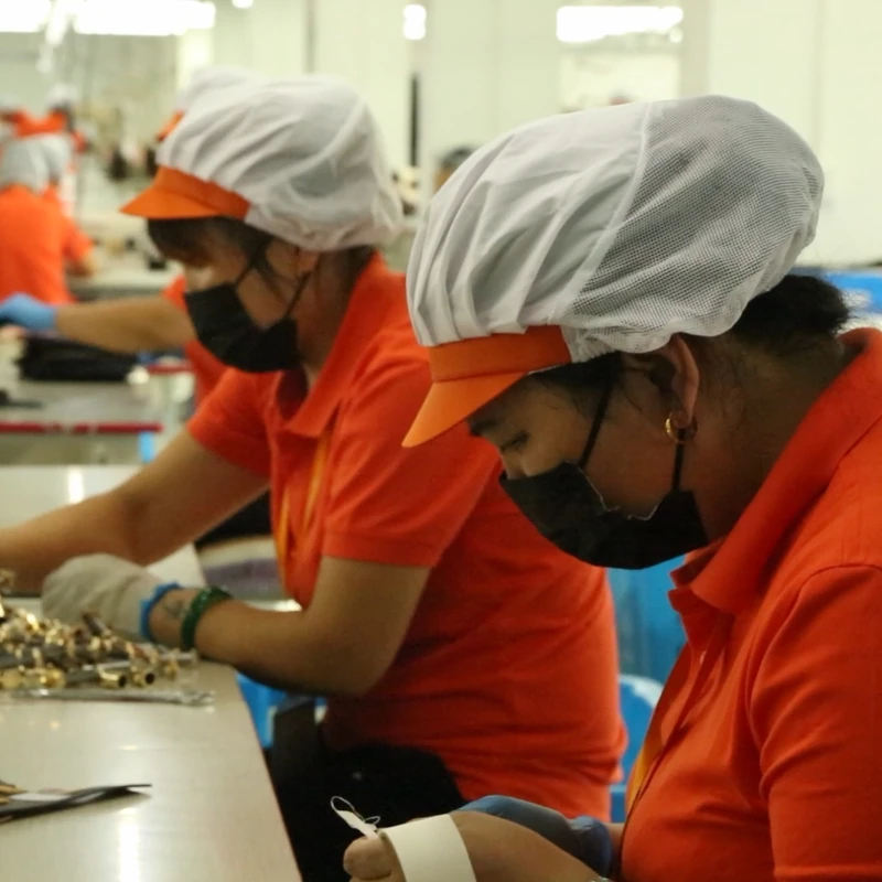 Workers handling small bag hardware and components at a production worktable.