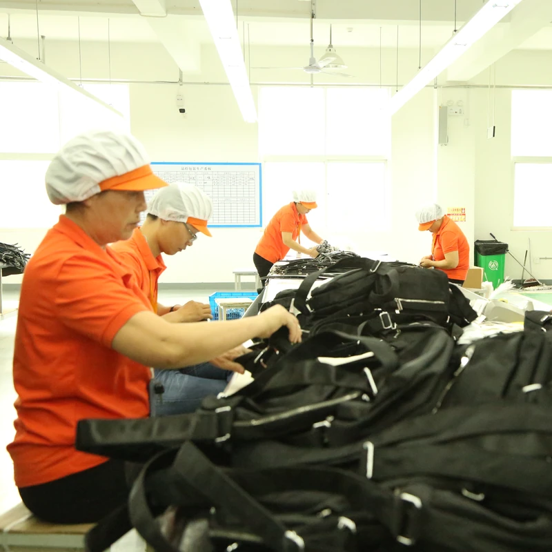 Workers handling black finished bags together at a factory worktable.