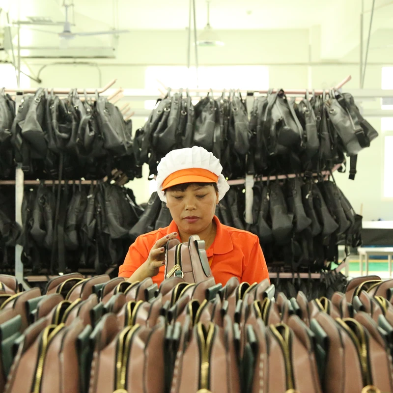 A worker handling finished bags arranged in rows at a factory worktable.