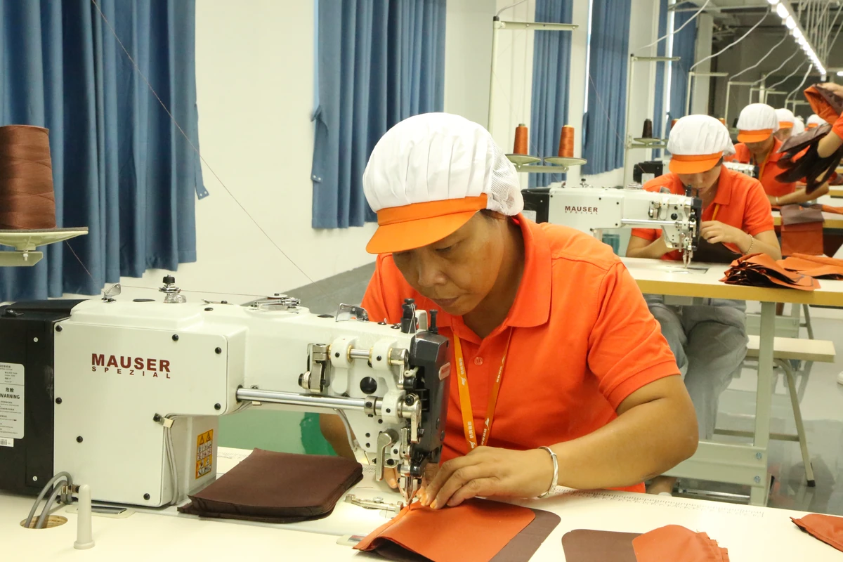 An operator guiding an orange bag panel through an industrial sewing machine.
