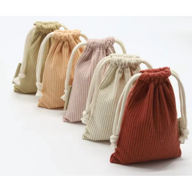 Five ribbed drawstring jewelry pouches in olive, peach, dusty mauve, cream and brick red with ivory cords.