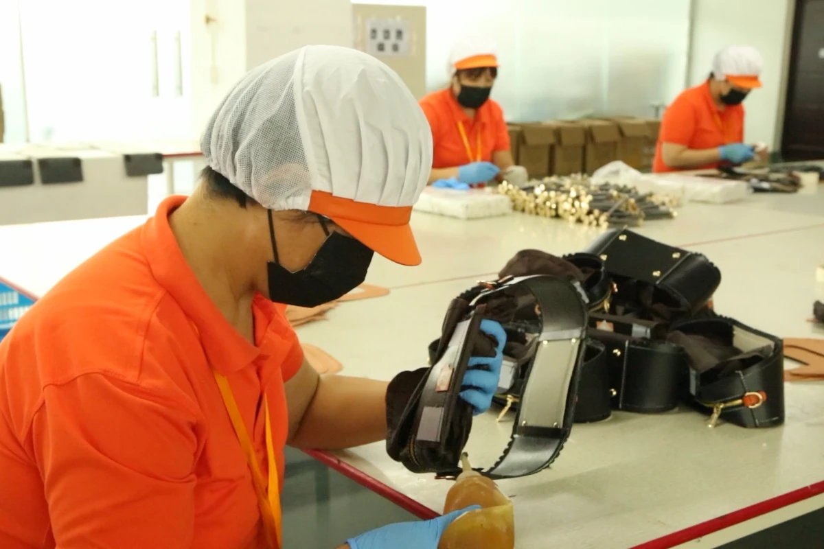 An operator handling a partly assembled bag at a shared worktable.