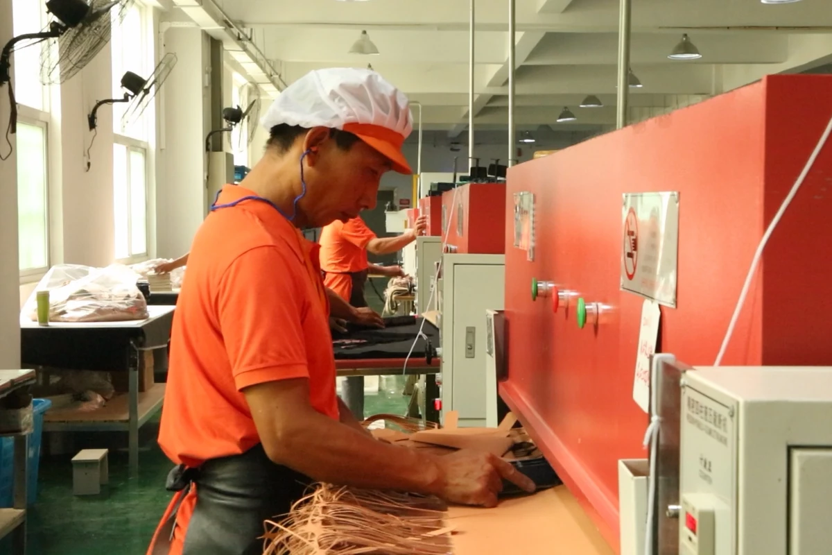 Operators handling bag components beside a row of workshop machines.