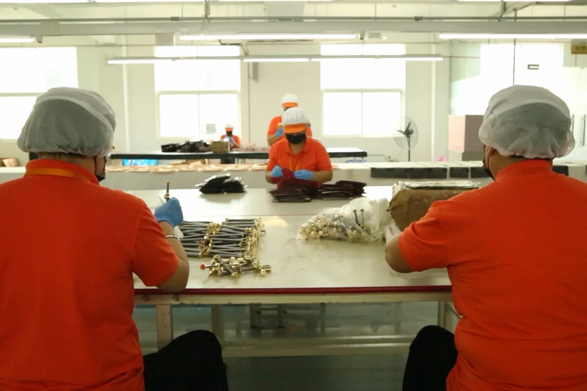 Workers handling bag components around a shared production table.
