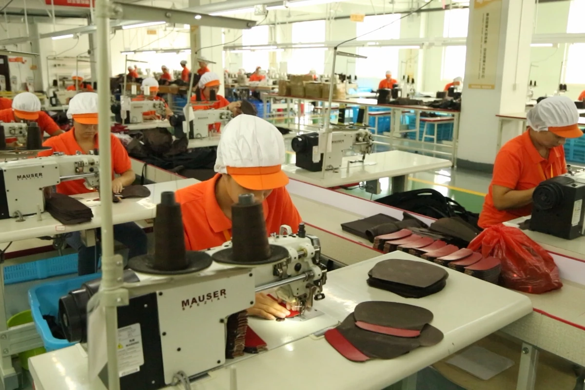 Sewing operators and prepared bag panels seen from above the worktables.