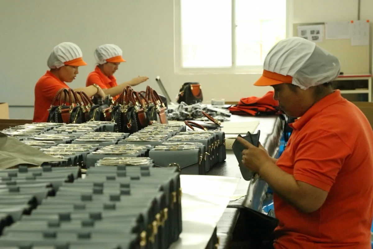 Workers handling small bags arranged in rows on a long worktable.