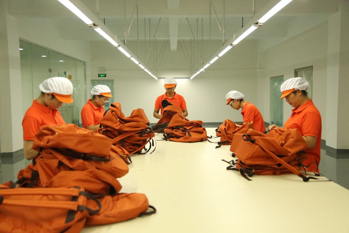 Workers handling orange bags around a shared finishing table.